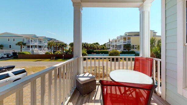 A balcony with a wicker chair and a small table, overlooking a residential area with multiple houses and a clear sky. - Paradise awaits! 7 Bedroom, Private Neighborhood Pool, Walk to the Beach! (Isle Of Palms)