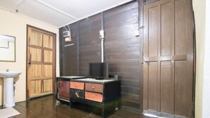 Quarto com guarda-roupa de madeira, escrivaninha com gavetas, televisão e prateleira na parede.