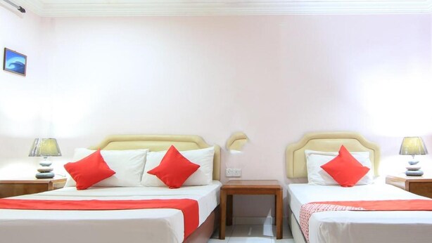 A hotel room with two beds, each with a red pillow, white bedding, and a wooden nightstand with a lamp. - Hotel O Ombak Inn Chalet (Pangkor Island)