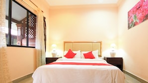 Quarto de hotel bem arrumado com uma cama grande, duas mesas de cabeceira com abajures e uma janela com cortinas.