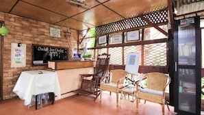 Interior de restaurante com balcão de recepção, móveis de vime e chão de azulejos.