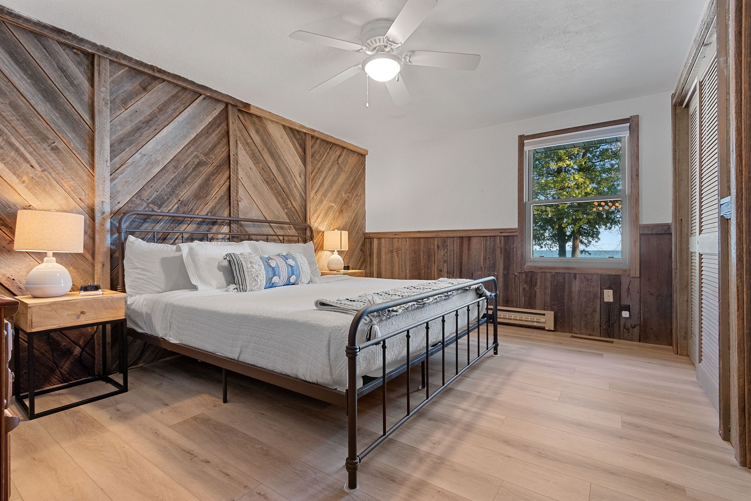 Ein Schlafzimmer mit Bett, Nachttischen, Deckenventilator, Fenster und Blick auf Bäume.