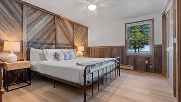 Ein Schlafzimmer mit Bett, Nachttischen, Deckenventilator, Fenster und Blick auf Bäume.