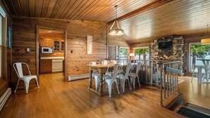 Un intérieur de chalet en bois spacieux, comprenant un coin repas, une cuisine et une cheminée en pierre.
