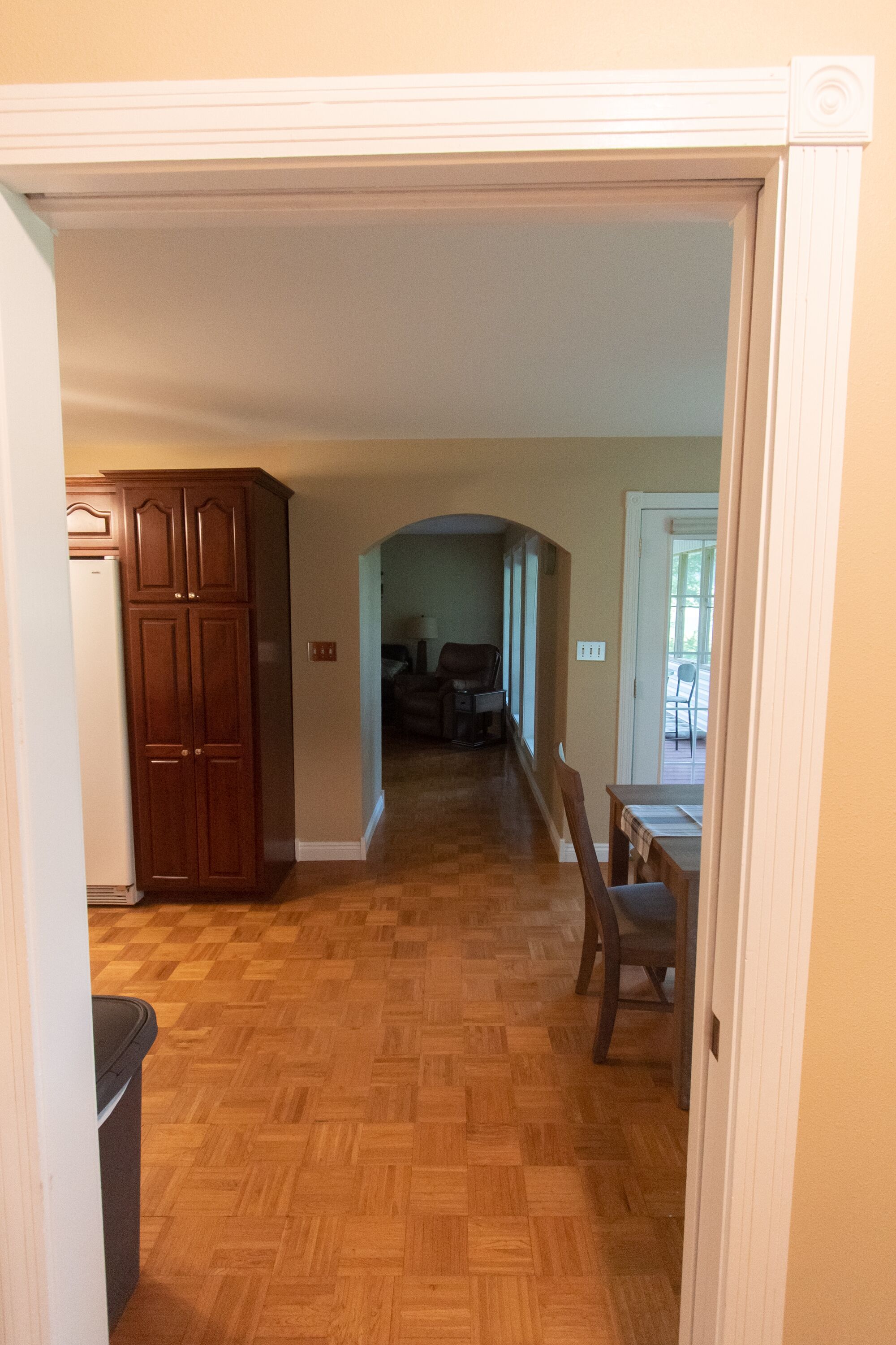 A hallway with wooden flooring leading to a dining area with a table and chairs.