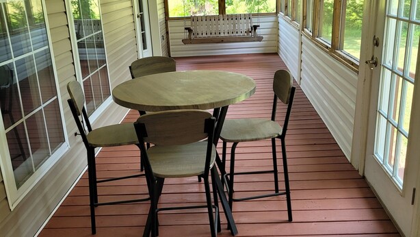 Eine überdachte Veranda mit Tisch, Stühlen und einer Bank, sowie großen Fenstern.