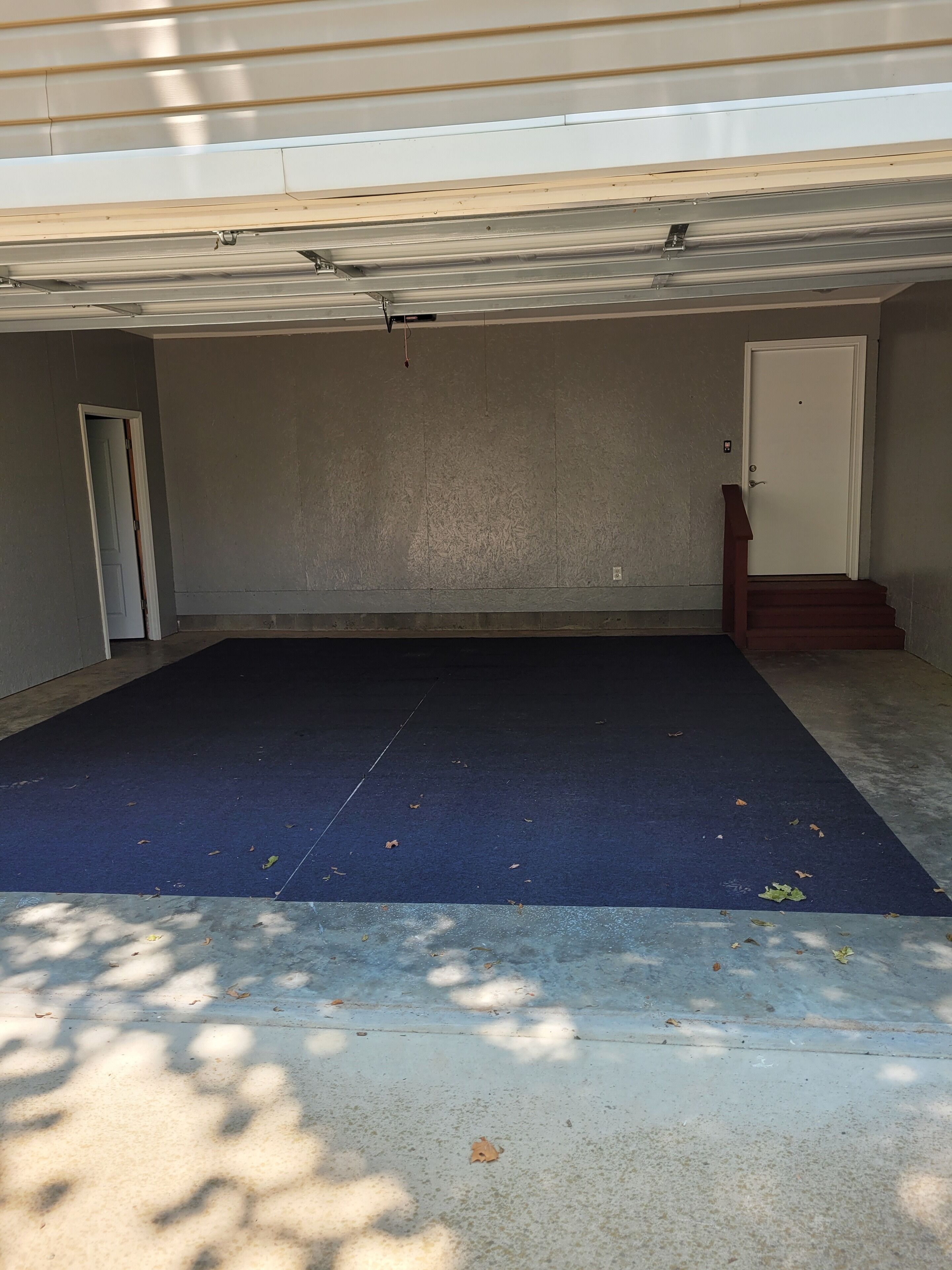 Un garatge amb un estriat blau, una porta blanca i una escala de fusta.