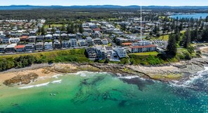 Vue aérienne d’une zone résidentielle côtière, avec de nombreux immeubles d’appartements, une côte rocheuse et des eaux turquoise limpides.