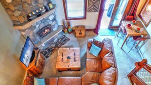 A cozy living room with a stone fireplace, leather sofa, wooden coffee table, and a dining area with a table and chairs.