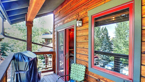 A wooden cabin with a covered porch, a sliding glass door, and a view of the surrounding forest.