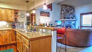 A kitchen with wooden cabinets, granite countertops, a stone fireplace, and pendant lighting.