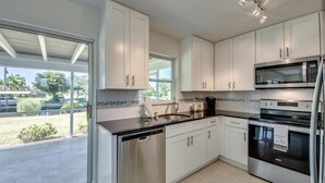 A modern kitchen with white cabinets, stainless steel appliances, and a large window offering a view of the outdoors. - Cozy in the Cape, Heated Saltwater Pool & Gulf access, water view  (Cape Coral)