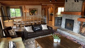 En hyggelig stue med pejs, lædersofa, træsofa og et mønstret tæppe.