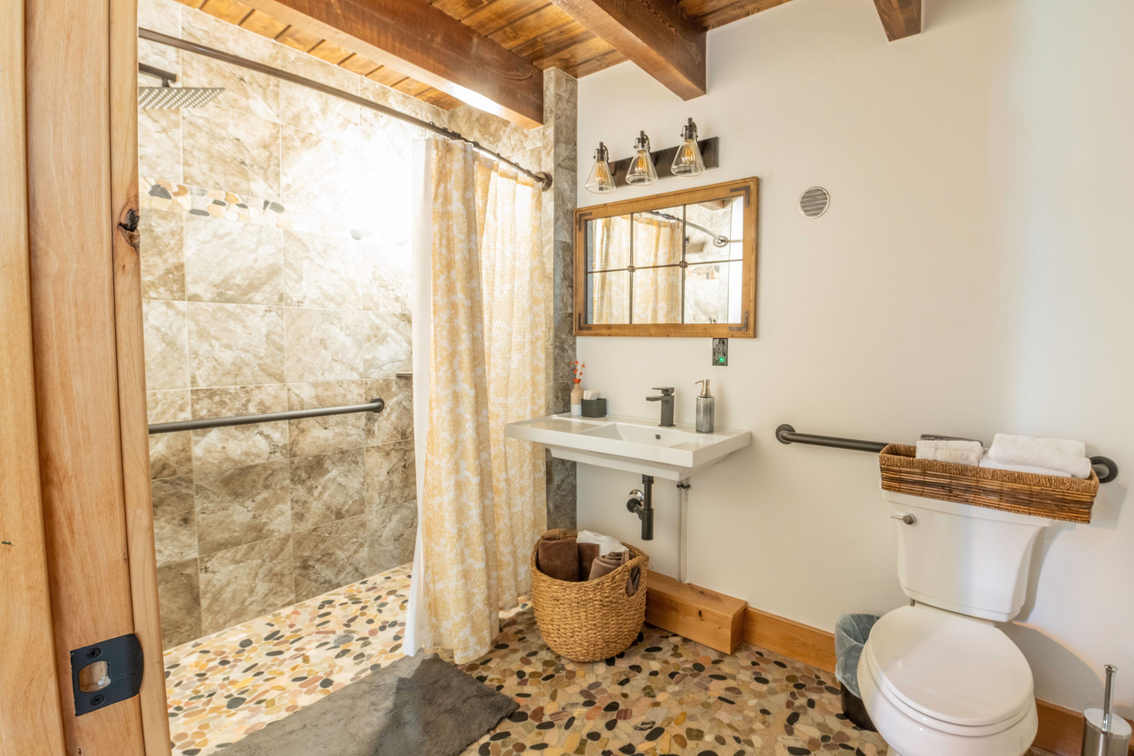 A bathroom with a shower, a sink, a toilet, and a mirror.