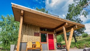 A rustic cabin with a red door, wooden exterior, and a covered porch. - Max's Cabin at Tiny Timbers Resort and Spa! (South Fork)