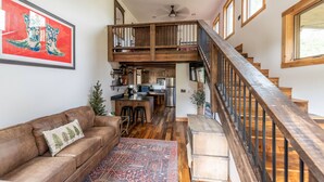 A spacious living area with a brown leather sofa, a patterned rug, and a wooden staircase with a railing. - Max's Cabin at Tiny Timbers Resort and Spa! (South Fork)