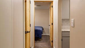 Un pasillo estrecho con puertas de madera, una cama al fondo y una zona de cocina a la derecha.