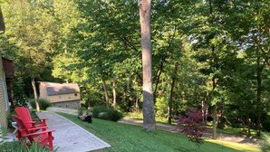 A backyard with a red Adirondack chair, a grill, and a small shed.