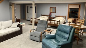 A bedroom with two beds, a sitting area with a sofa and chairs, a wooden table, and a large window.