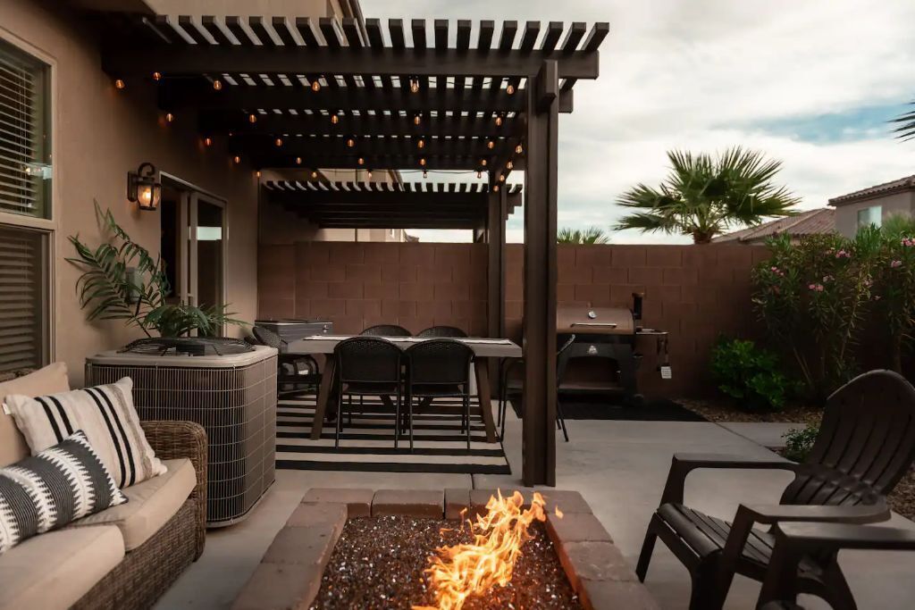 An outdoor patio with a fire pit, seating area, and a pergola with string lights.