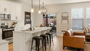 Una cocina moderna con armarios blancos, una isla central con taburetes, horno empotrado y una lámpara colgante.