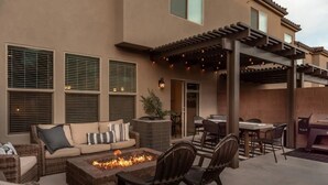 Un patio al aire libre con un brasero, una zona de estar y una pérgola con luces colgantes.