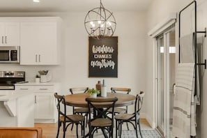 A modern kitchen with white cabinetry, a dining table with six chairs, and a chandelier.