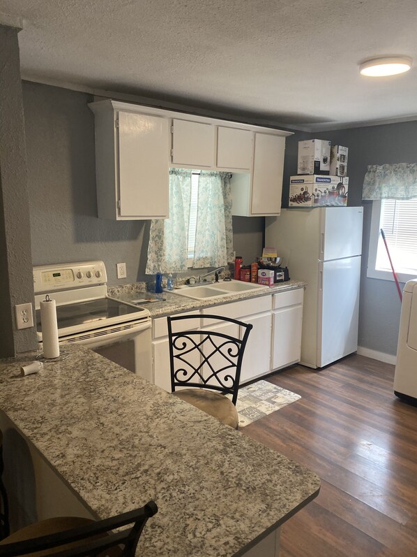 A compact kitchen with white cabinets, a granite countertop, a built-in oven, and a refrigerator. - Cozy 2 bedroom (Dallas)