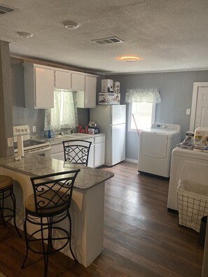 A compact kitchen with white cabinets, a built-in stove, a sink, and a small dining area with a bar stool. - Cozy 2 bedroom (Dallas)