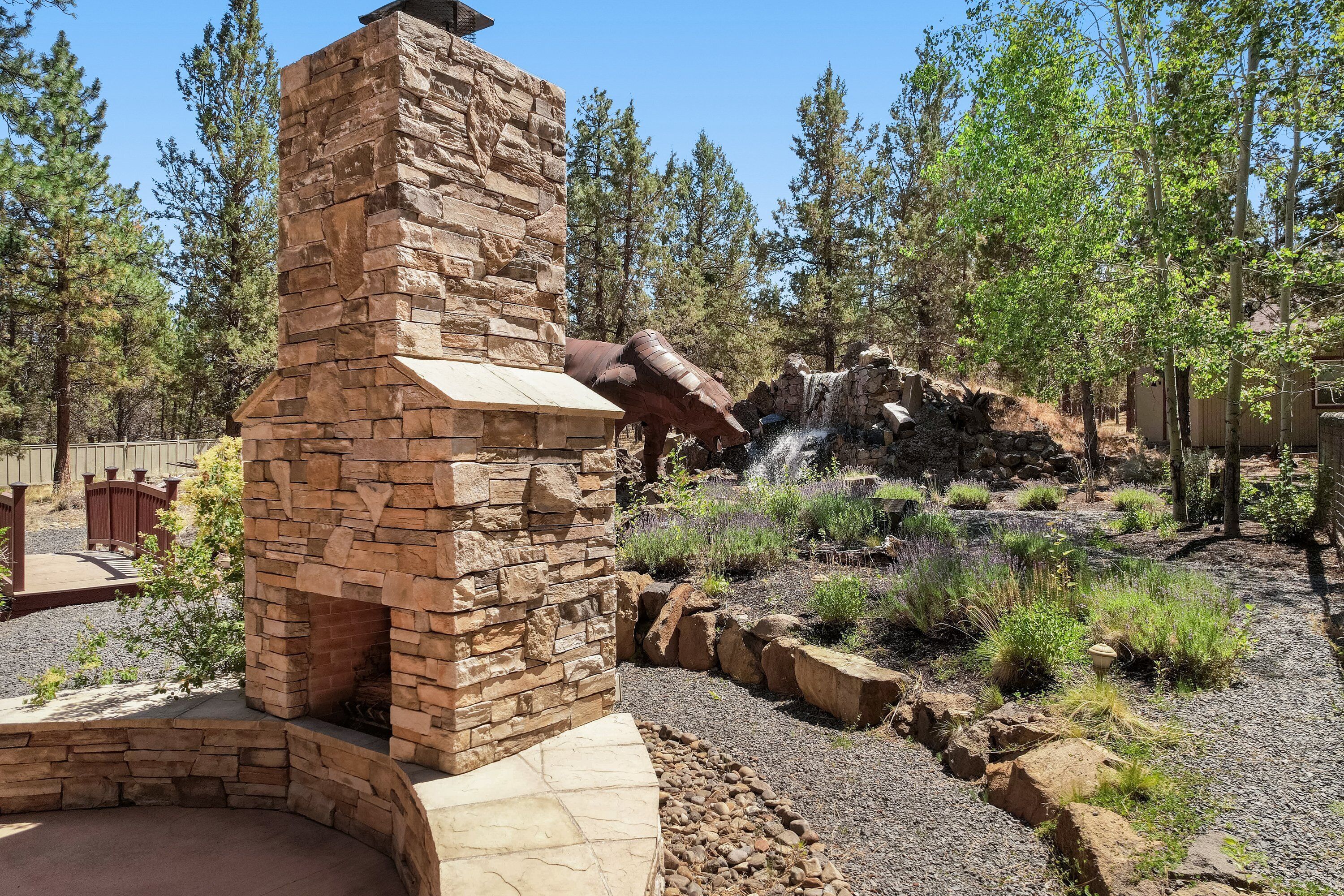 A stone fireplace with a chimney, surrounded by a landscaped garden with various plants and a small waterfall feature.