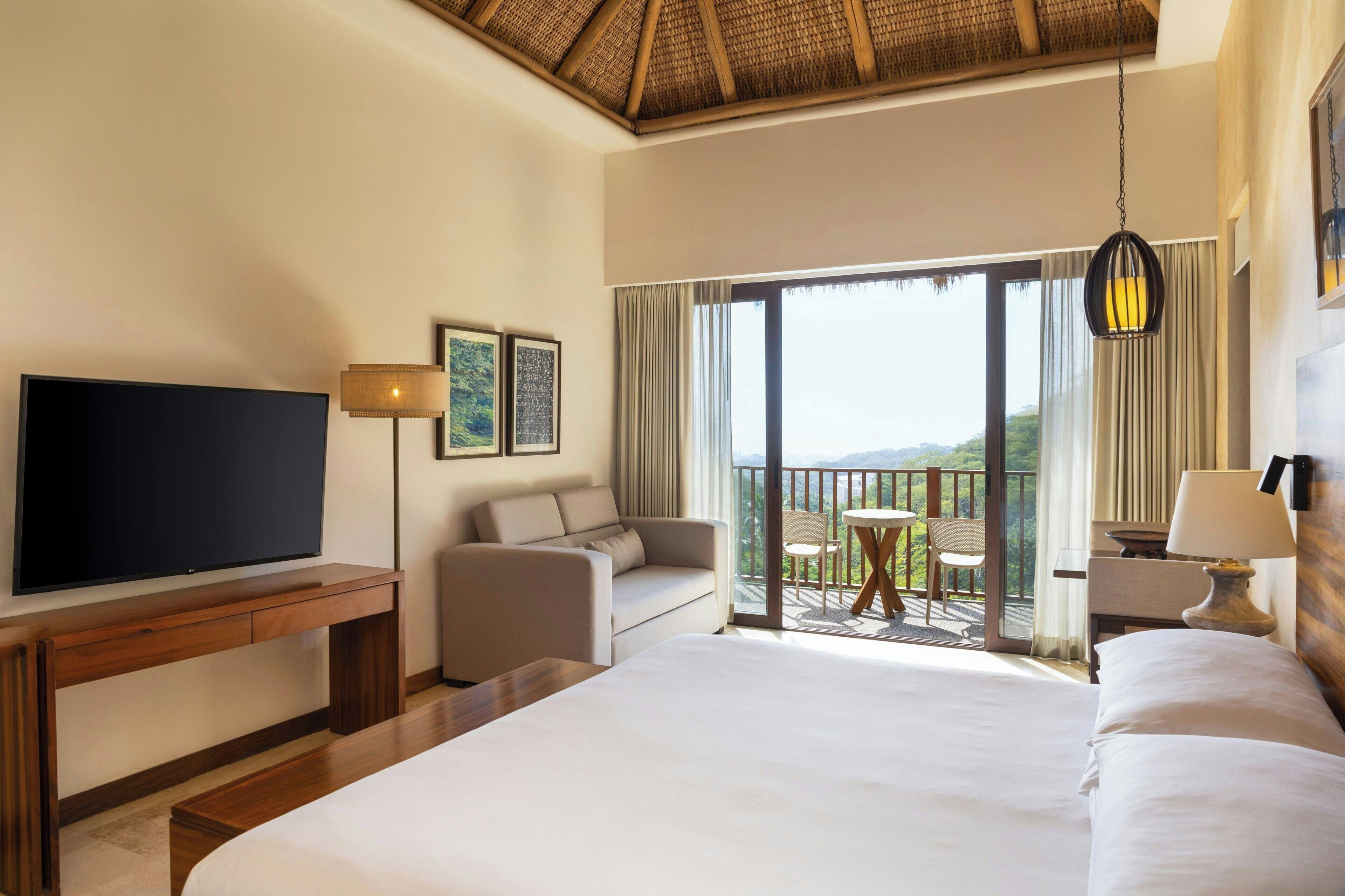 A hotel room with a large bed, a TV, a sofa, a desk, and a balcony with a view.