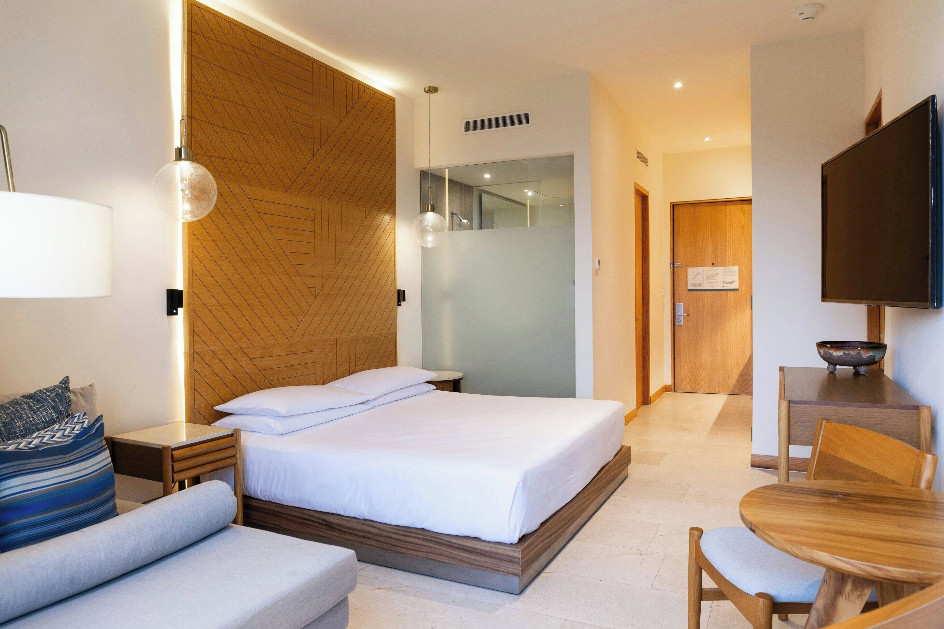 Ein modernes Hotelzimmer mit Bett, Sofa, Esstisch und Fernseher.
