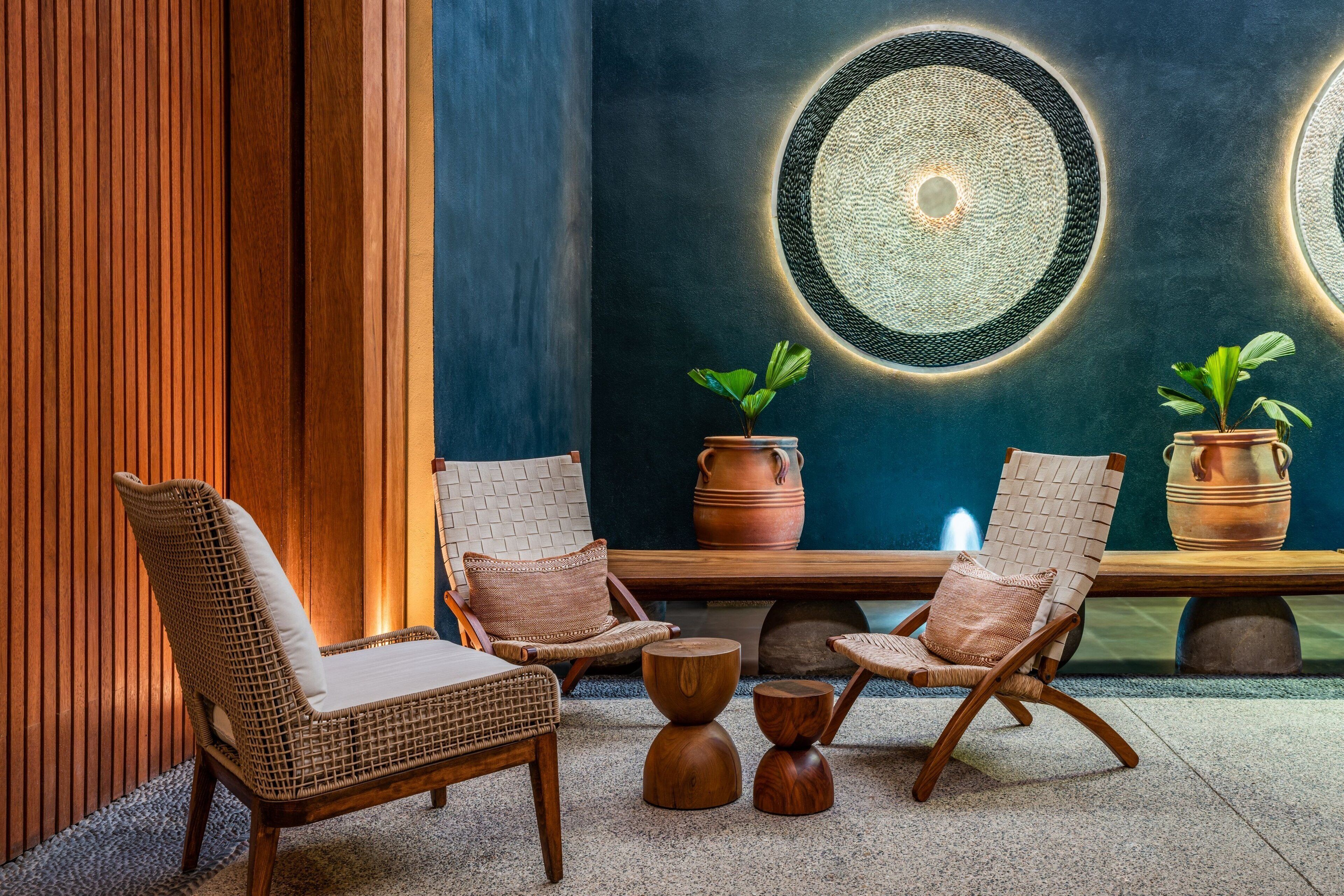 Een moderne loungehoek met rieten stoelen, een houten bank en potplanten.