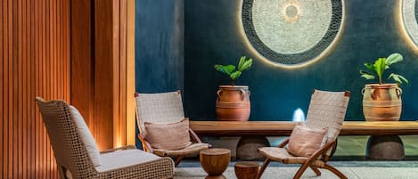 Een moderne loungehoek met rieten stoelen, een houten bank en potplanten.