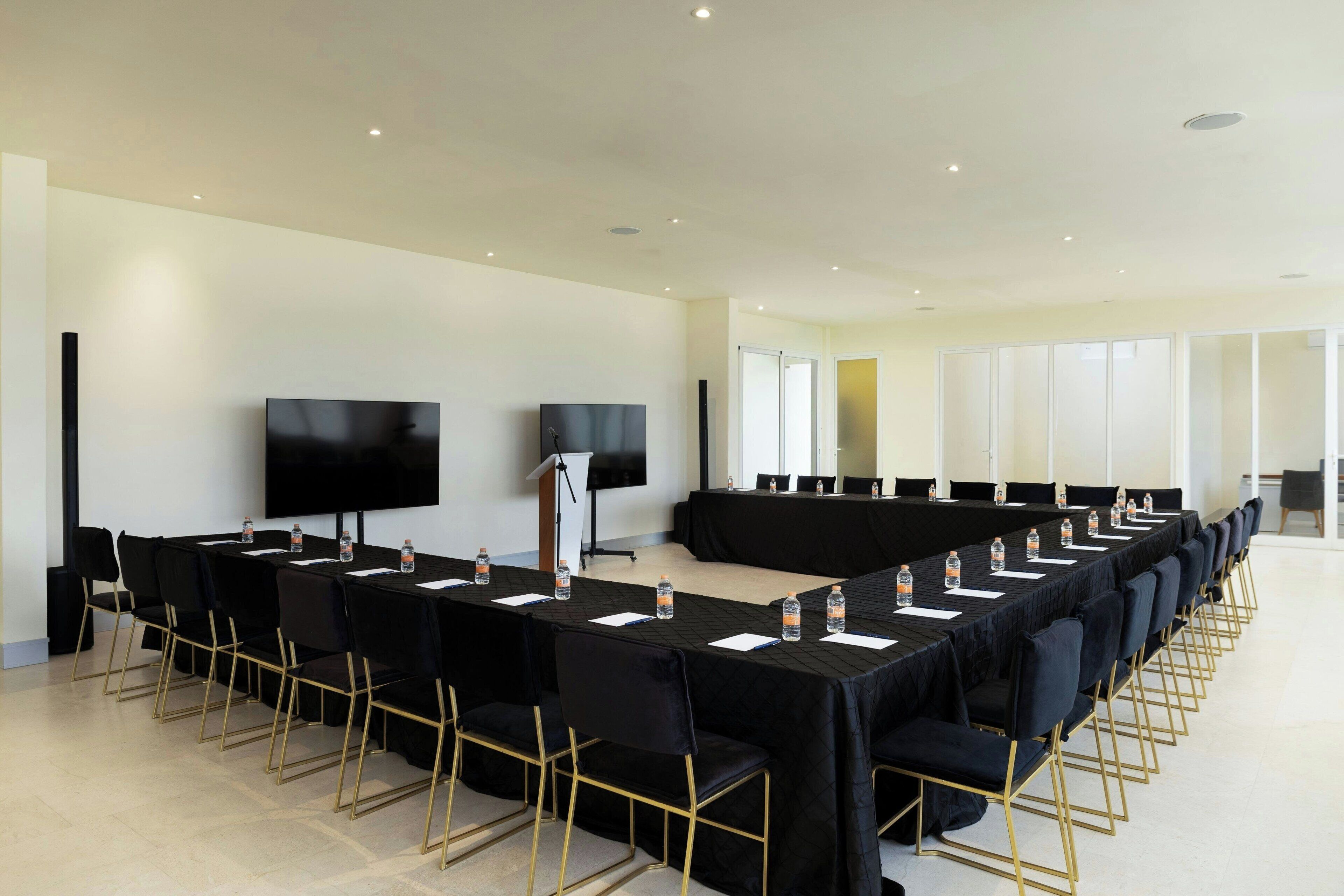 Un salón de conferencias con una larga mesa, sillas, un atril y una pantalla grande.