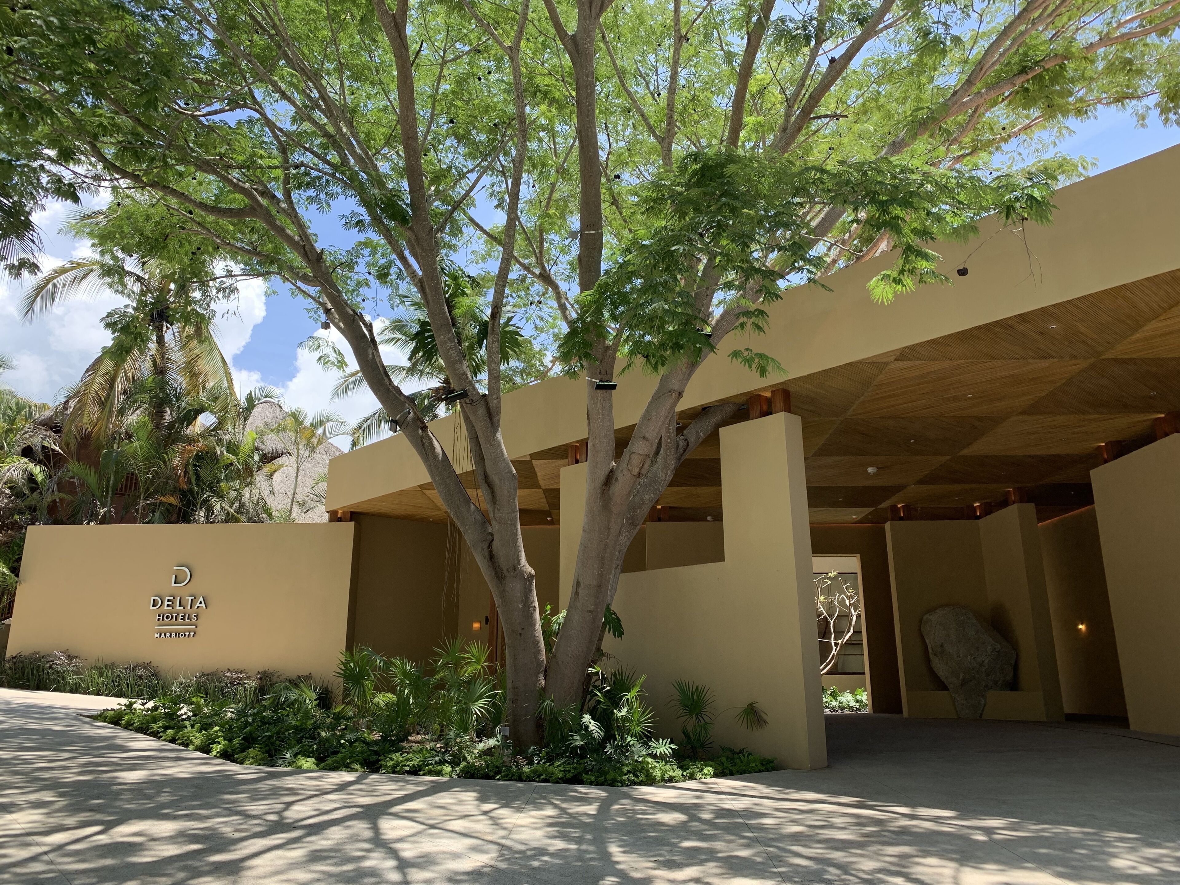 The exterior of a Delta Hotels Marriott building with a modern architectural design, surrounded by lush greenery and palm trees.