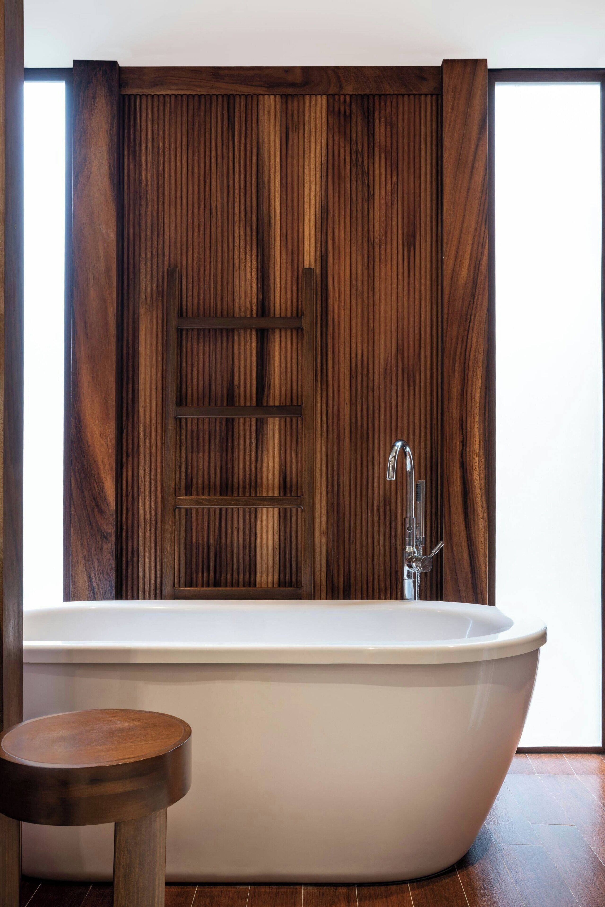 Une salle de bain moderne avec une baignoire sur pieds, un mur recouvert de panneaux en bois et un petit tabouret en bois.