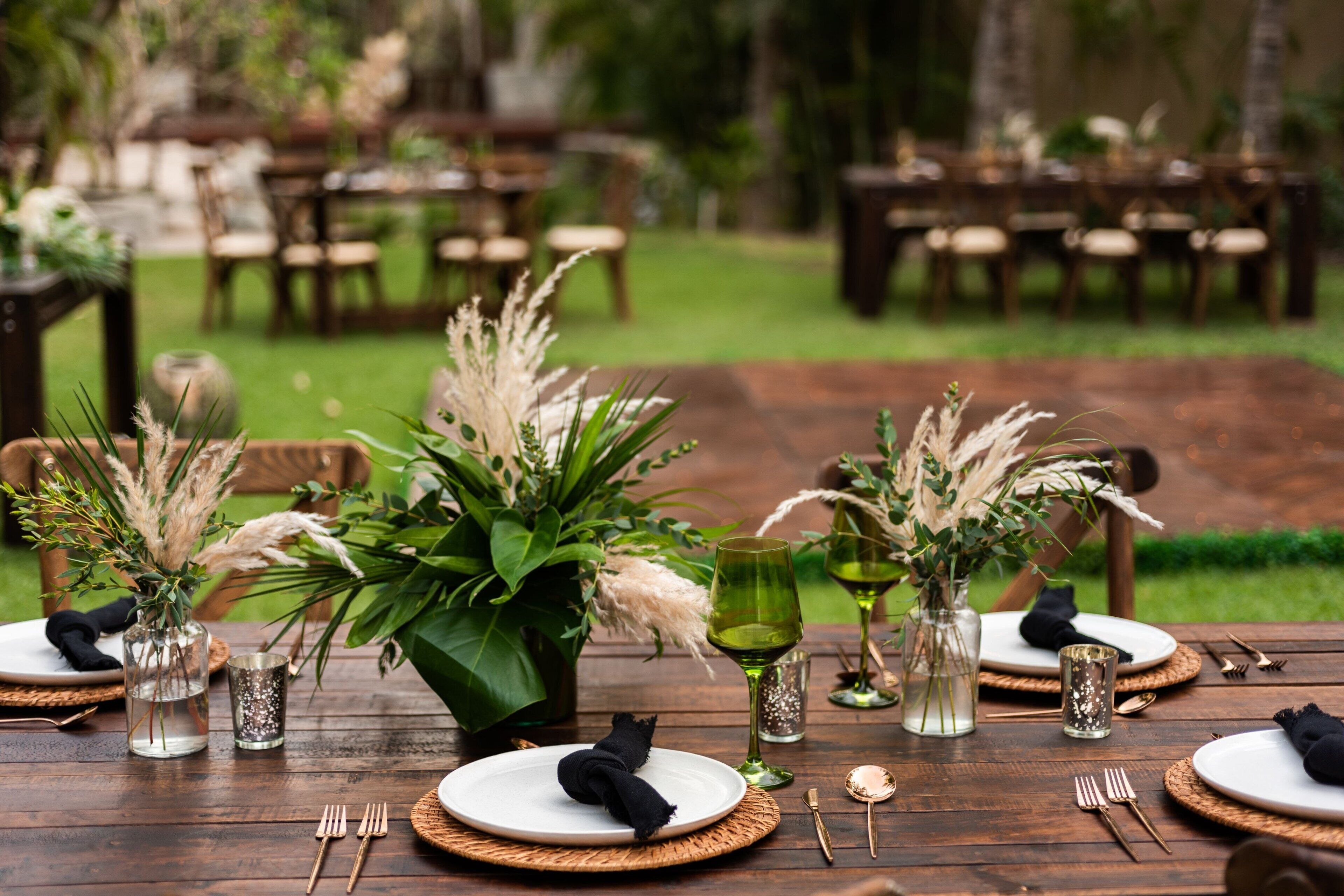 A wooden outdoor dining table set with plates, cutlery, and decorative plants.