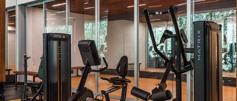 Une salle de sport équipée de divers appareils d’exercice, dotée de grandes fenêtres et d’un plancher en bois.