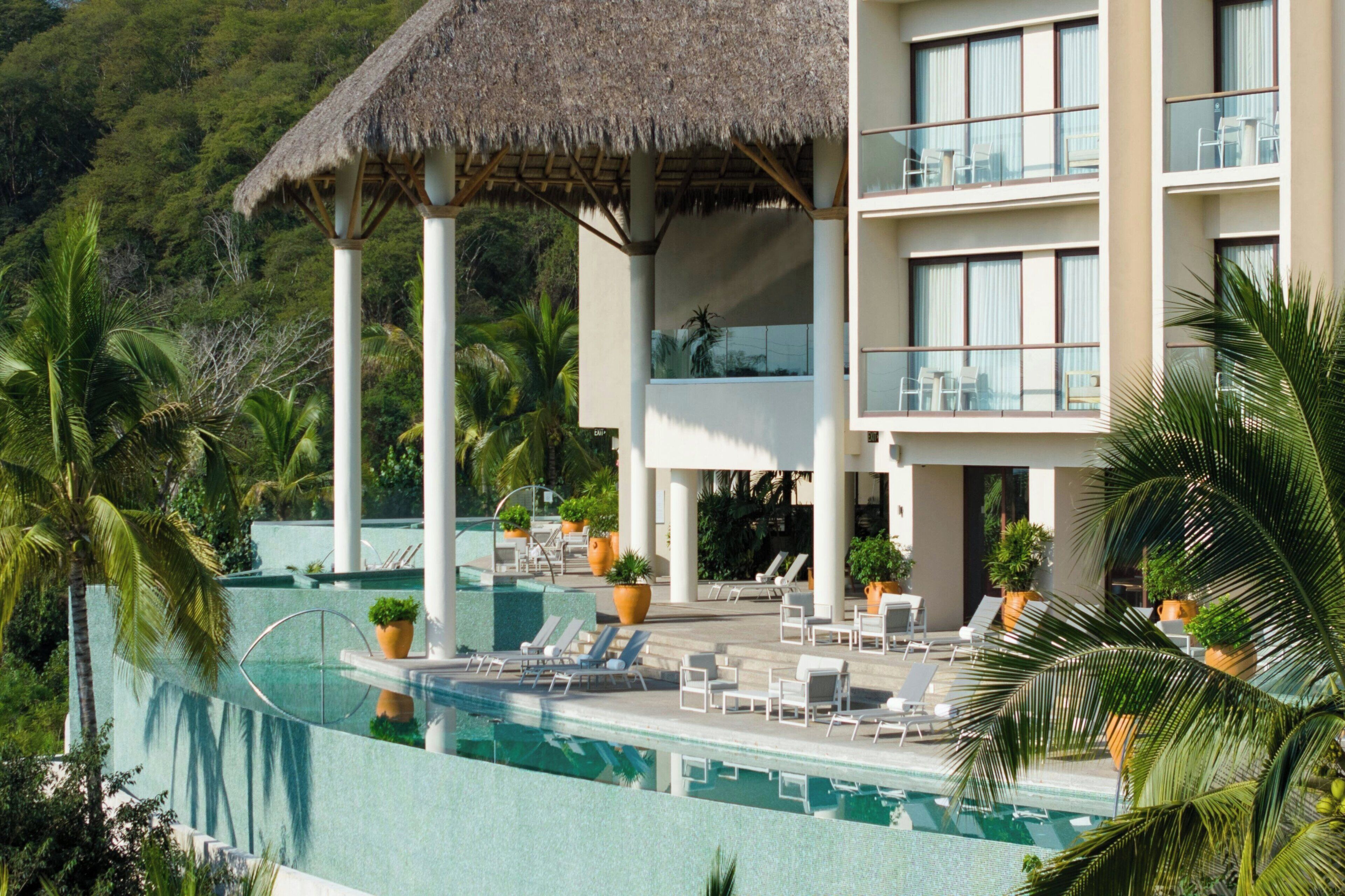 A resort with a infinity pool, lounge chairs, and a thatched-roof structure.
