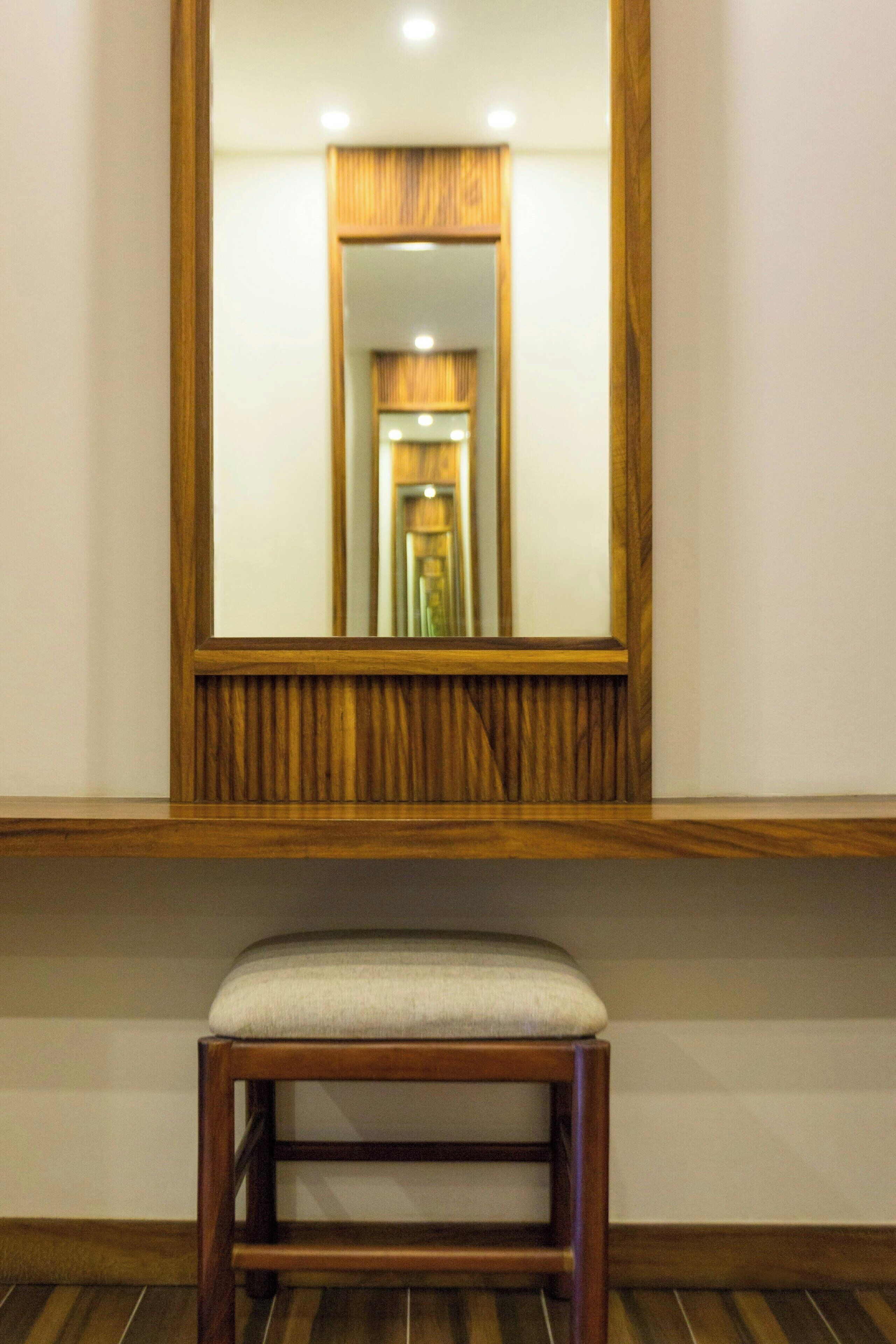 Un miroir à cadre en bois, avec un tabouret placé devant.