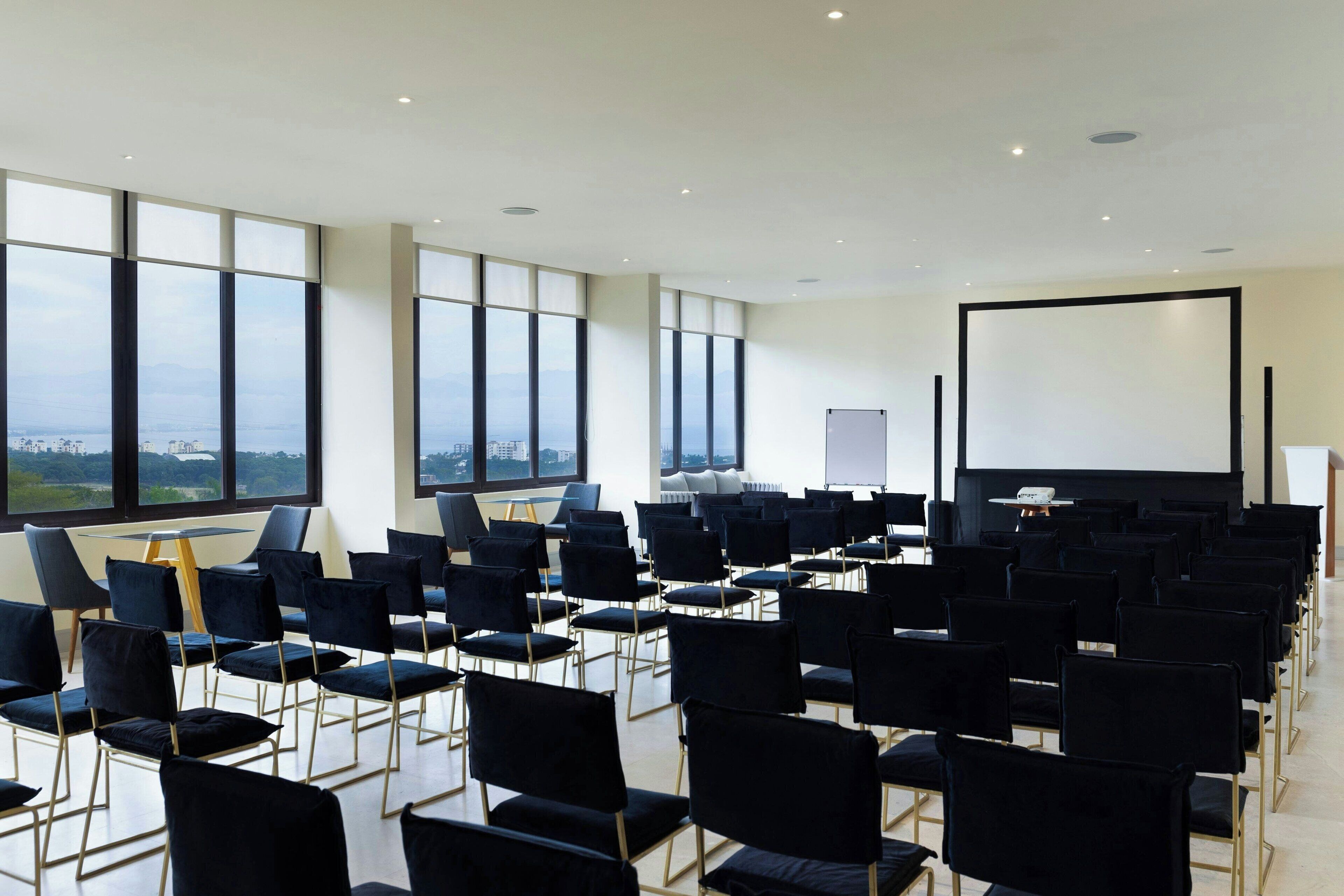 A conference room with rows of black chairs, a large screen, and a projector.