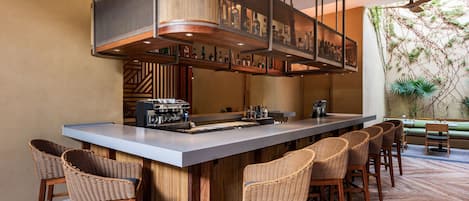 Una zona de bar con una barra larga, taburetes de mimbre y un ventilador de techo.