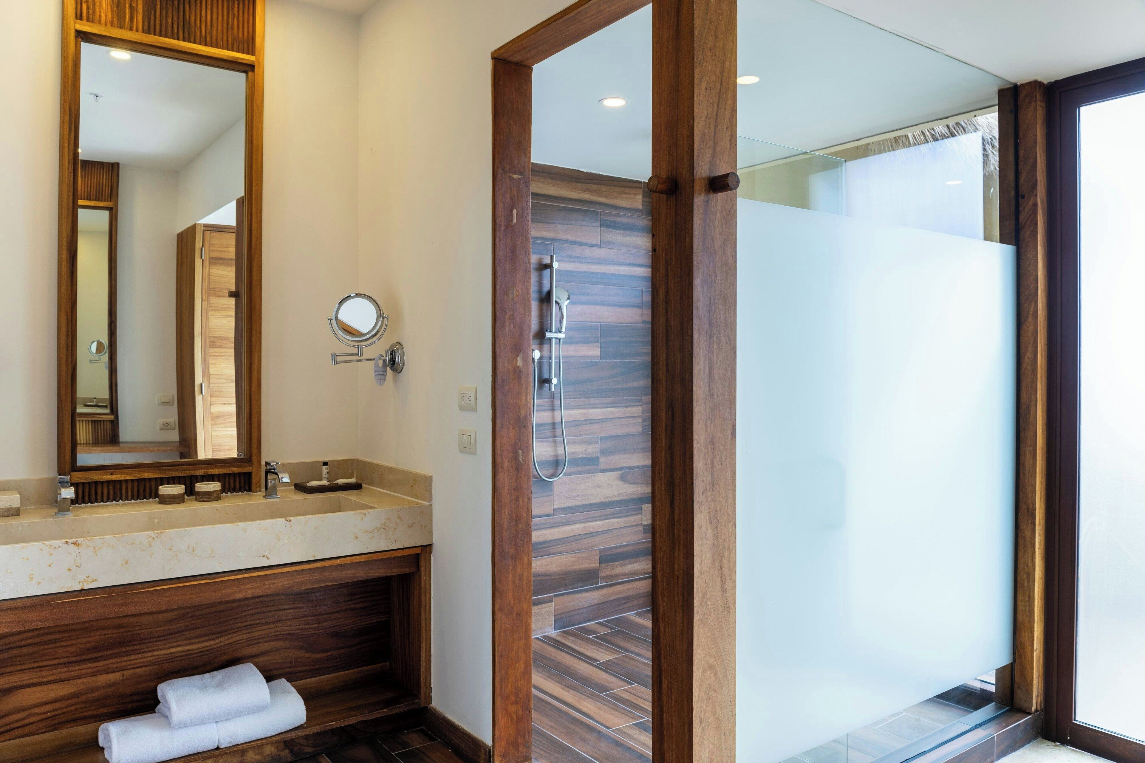A modern bathroom with a wooden vanity, a large mirror, a glass shower enclosure, and a visible towel rack.