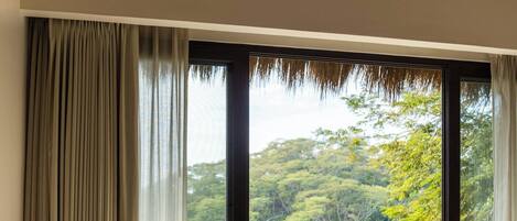 Habitación con sofá, una mesa y sillas en un balcón con vista a zona boscosa.