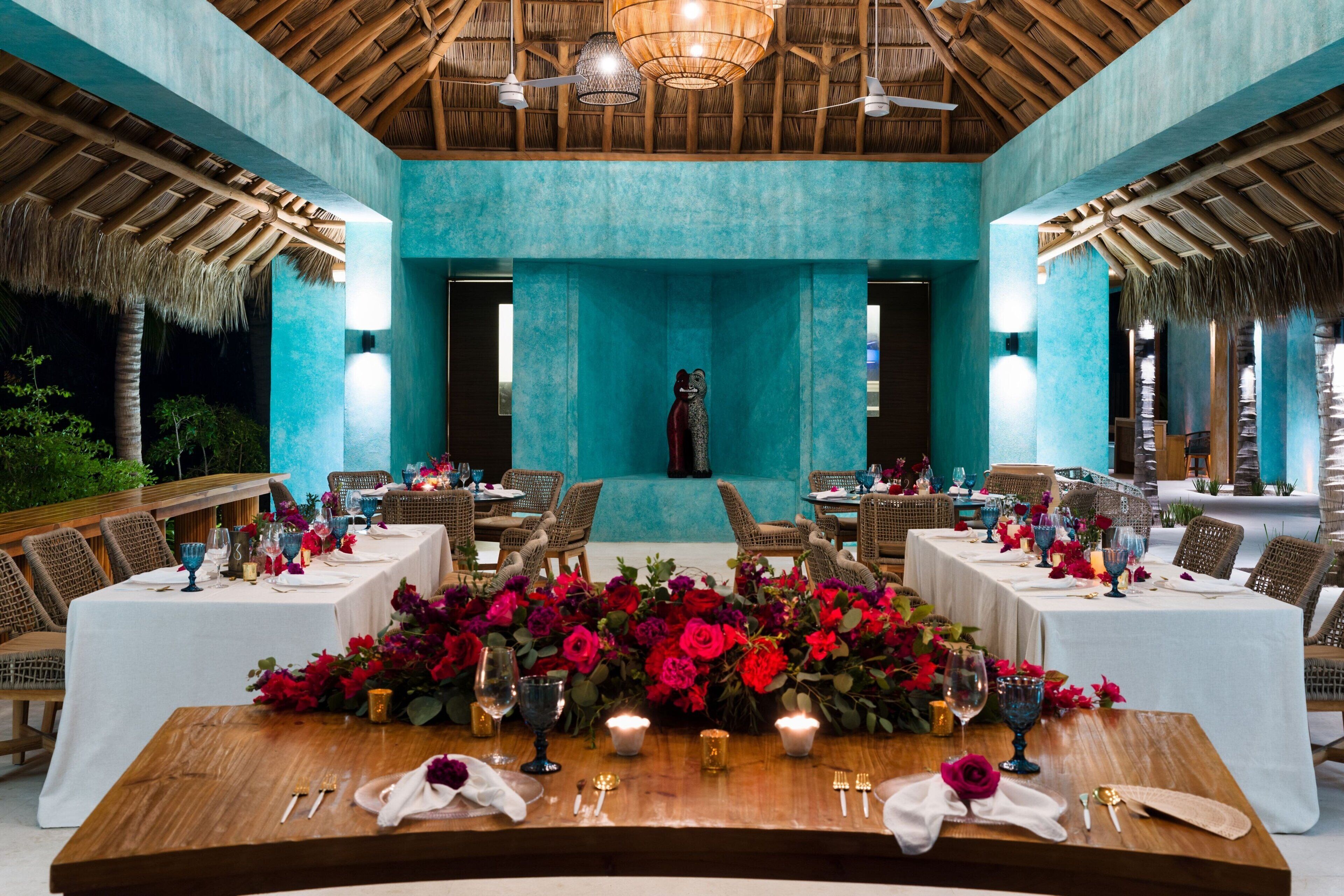 Comedor con mesas dispuestas para una comida, destacando un arreglo floral central y una vista de una piscina al fondo.