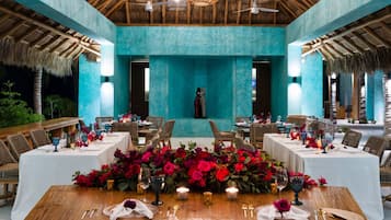 Comedor con mesas dispuestas para una comida, destacando un arreglo floral central y una vista de una piscina al fondo.