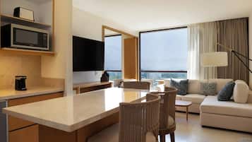 Una habitación de hotel moderna con cocina, una mesa de comedor con sillas, un sofá y un amplio ventanal con vistas.