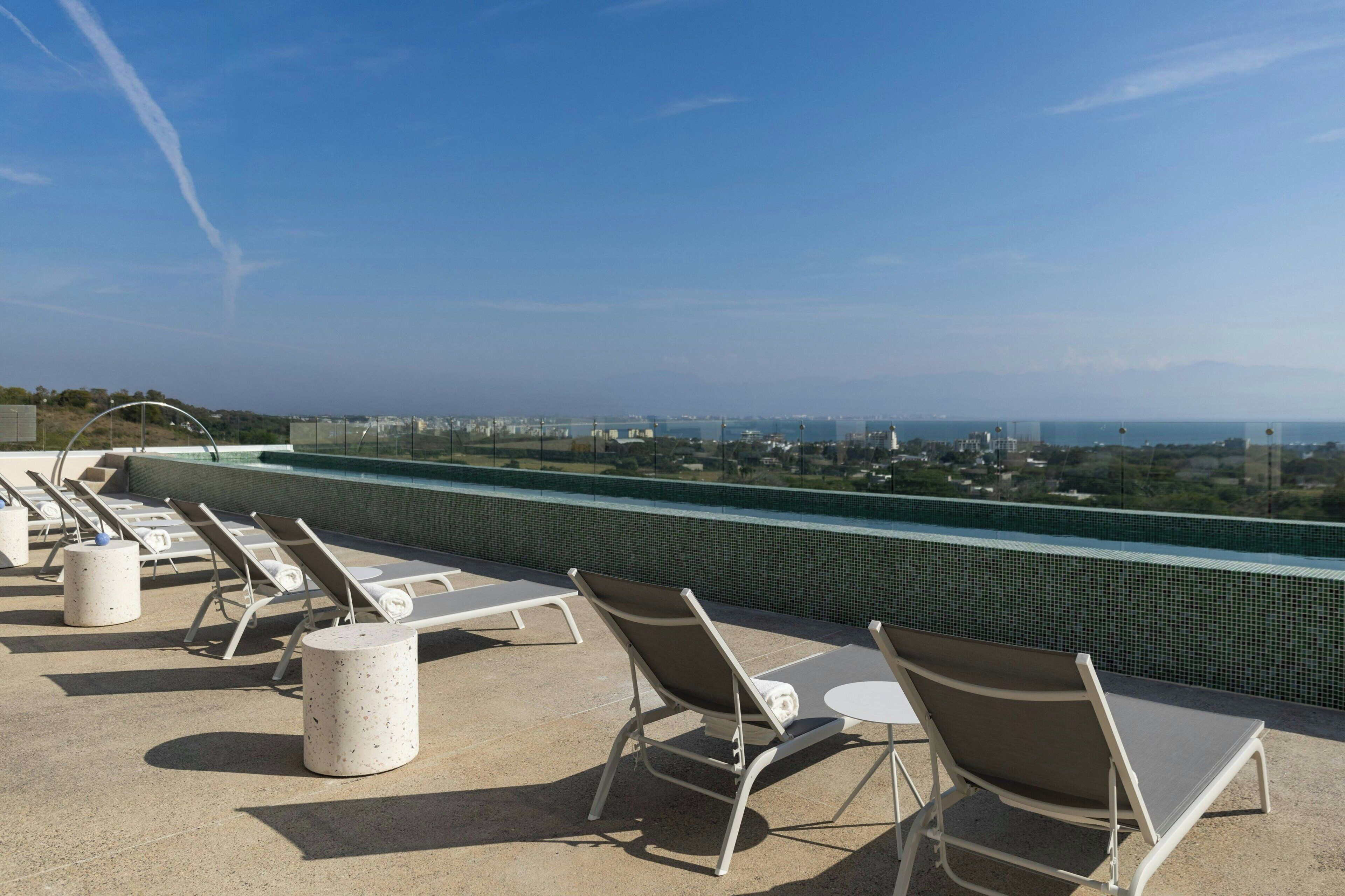 Un área de piscina en la azotea con sillones de descanso y vistas de la ciudad.