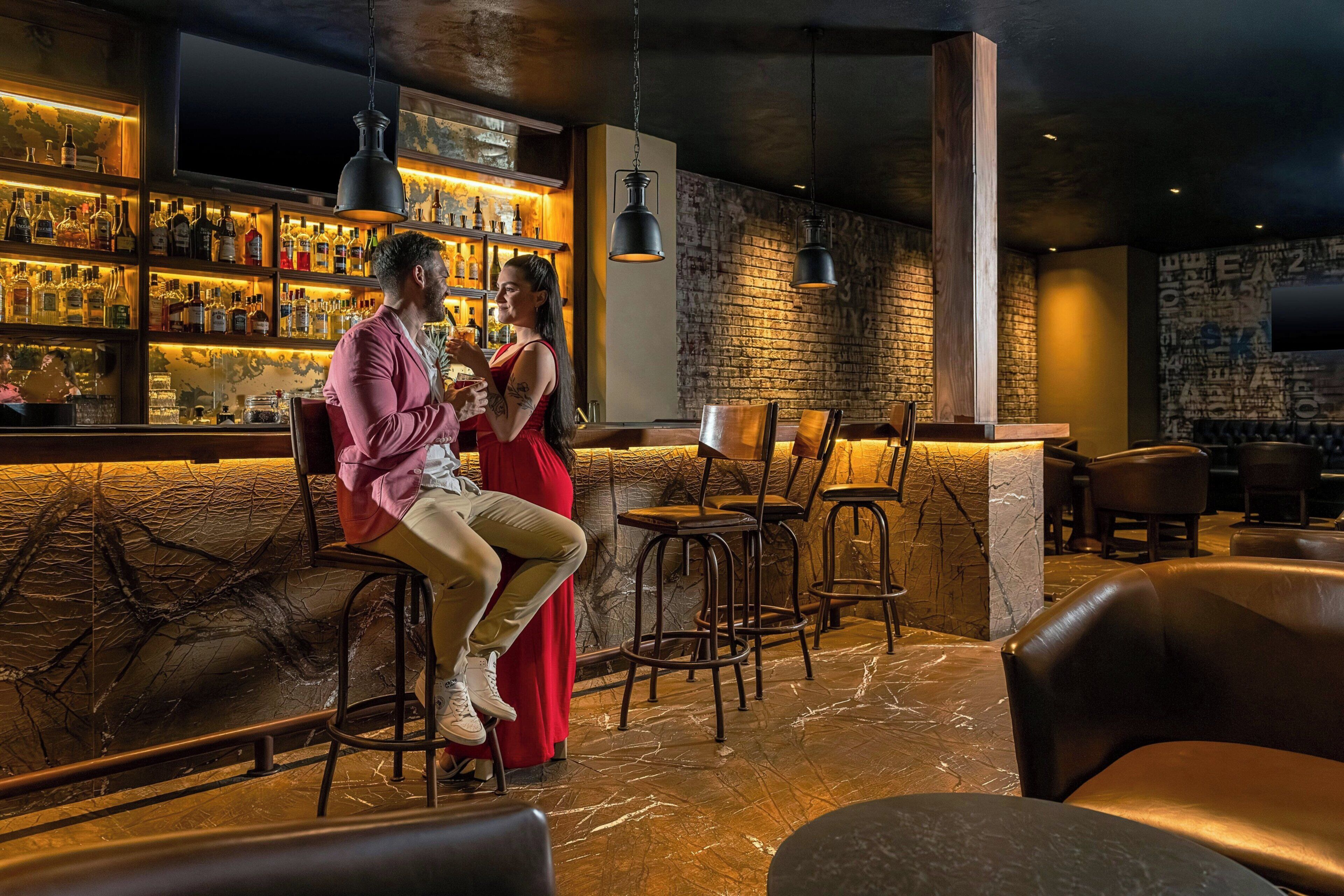 Un espace bar avec un mur en briques, des luminaires suspendus et une variété de bouteilles.